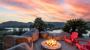 Un foyer avec des chaises rouges, de gros rochers et une vue magnifique sur les montagnes et un lac au coucher du soleil.