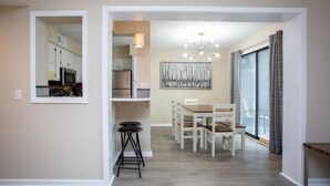 Un comedor con una mesa y sillas, una lámpara colgante y vistas de la cocina a través de un vano abierto.