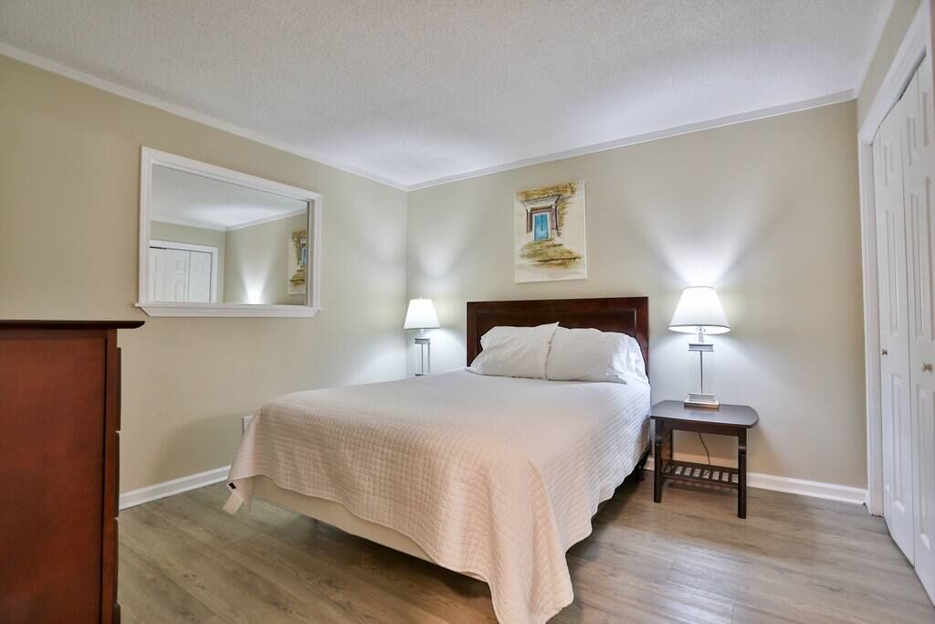 A bedroom with a bed, two bedside lamps, a nightstand, a mirror, and a door.