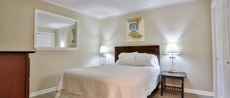 A bedroom with a bed, two bedside lamps, a nightstand, a mirror, and a door.