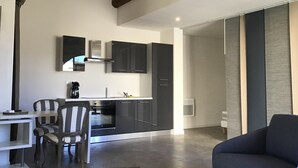 Una cocina moderna con armarios oscuros, horno empotrado y cafetera. Hay un rincón de comedor con una silla a rayas y un sofá.