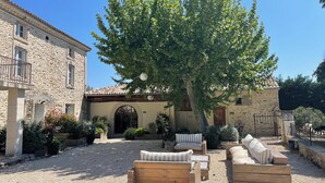 Un patio con edificios de piedra, un árbol grande y mobiliario para exteriores.