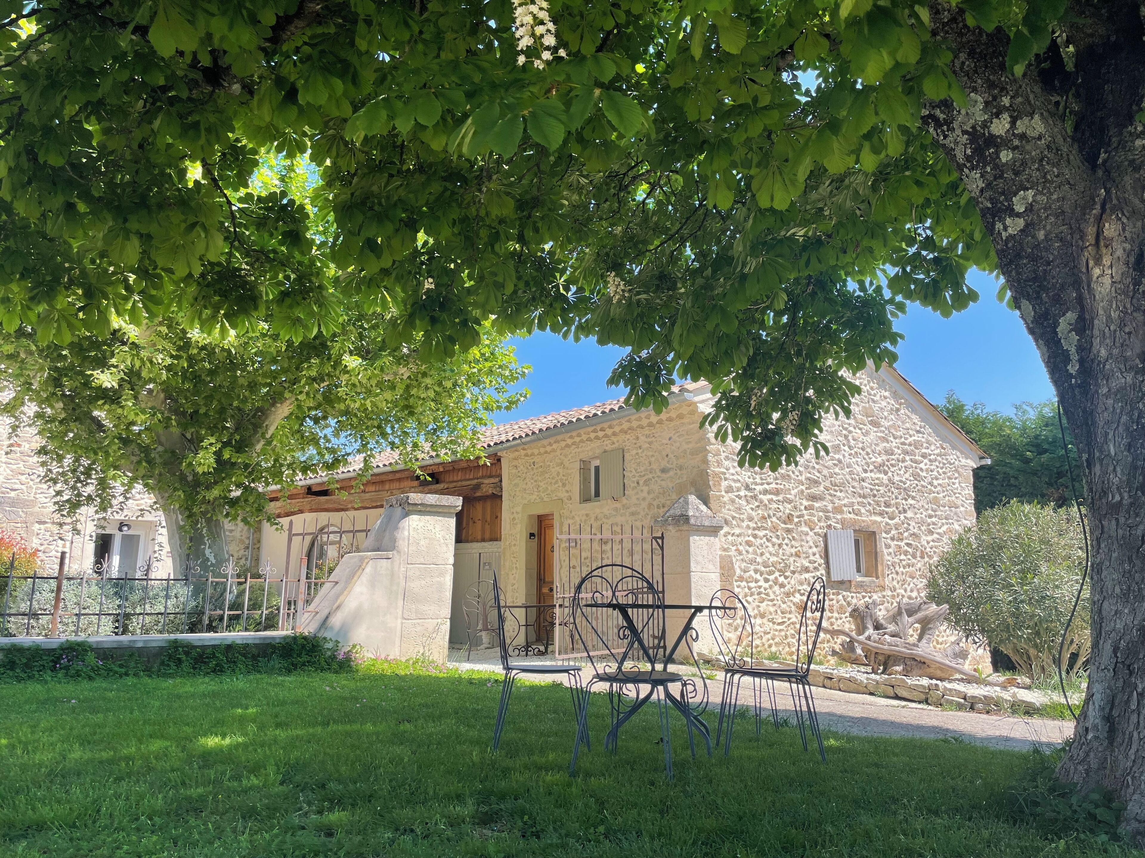 A stone building with a tiled roof, a grassy lawn, and a metal gate.