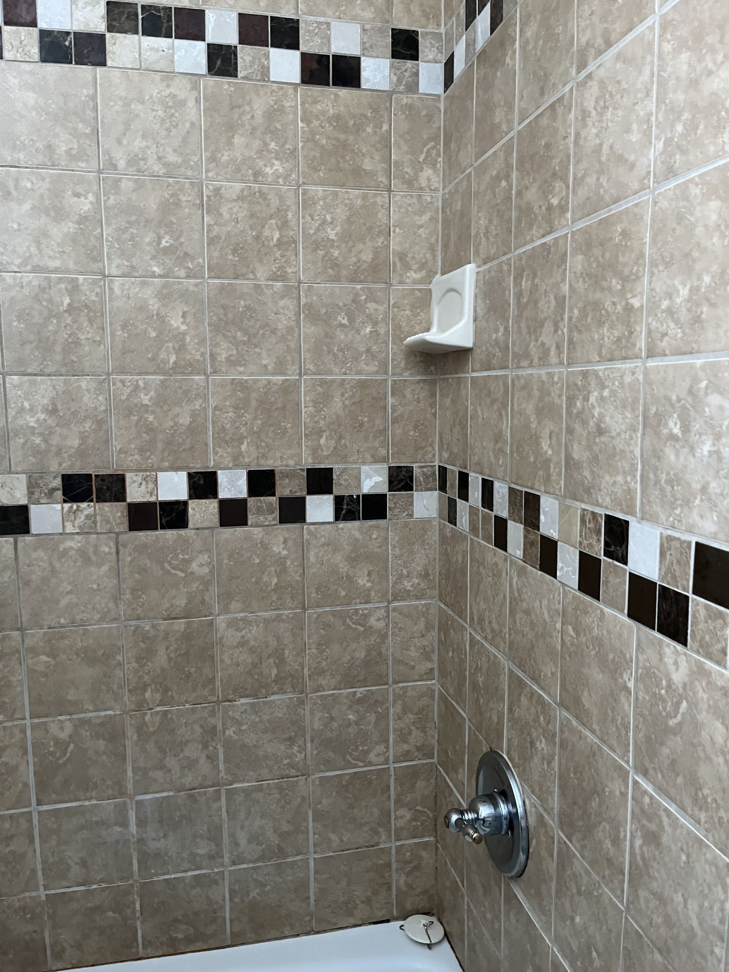 Un baño con baldosas color beige, un inodoro blanco y una ducha con grifo cromado.