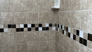 Un baño con baldosas color beige, un inodoro blanco y una ducha con grifo cromado.
