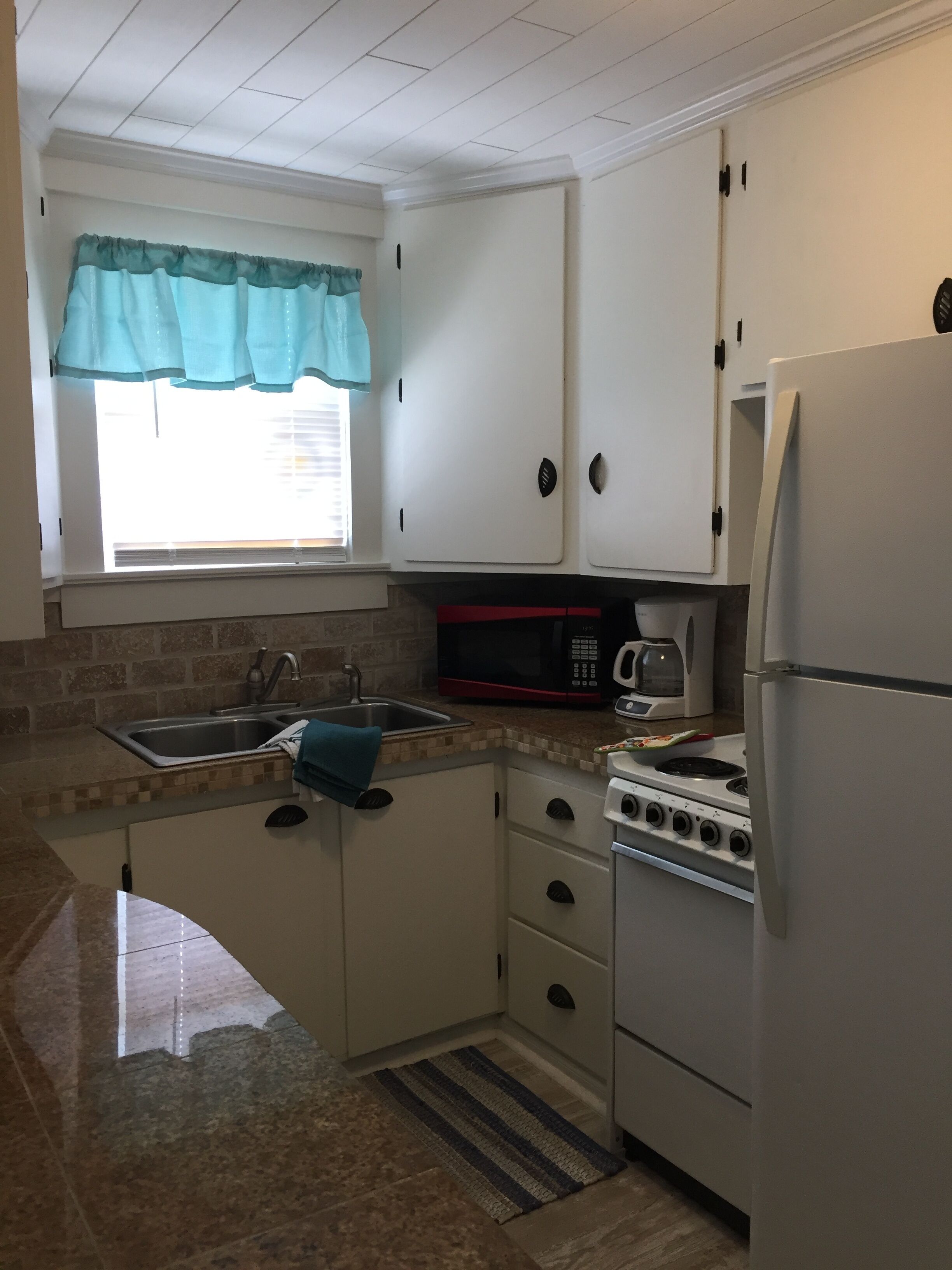 Una cocina compacta con armarios blancos, un lavamanos de acero inoxidable, un microondas, una estufa y un refrigerador.