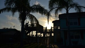 Rakennuksessa on parveke, jolta avautuu näkymä vehreälle alueelle, palmuille ja auringonlaskuun.