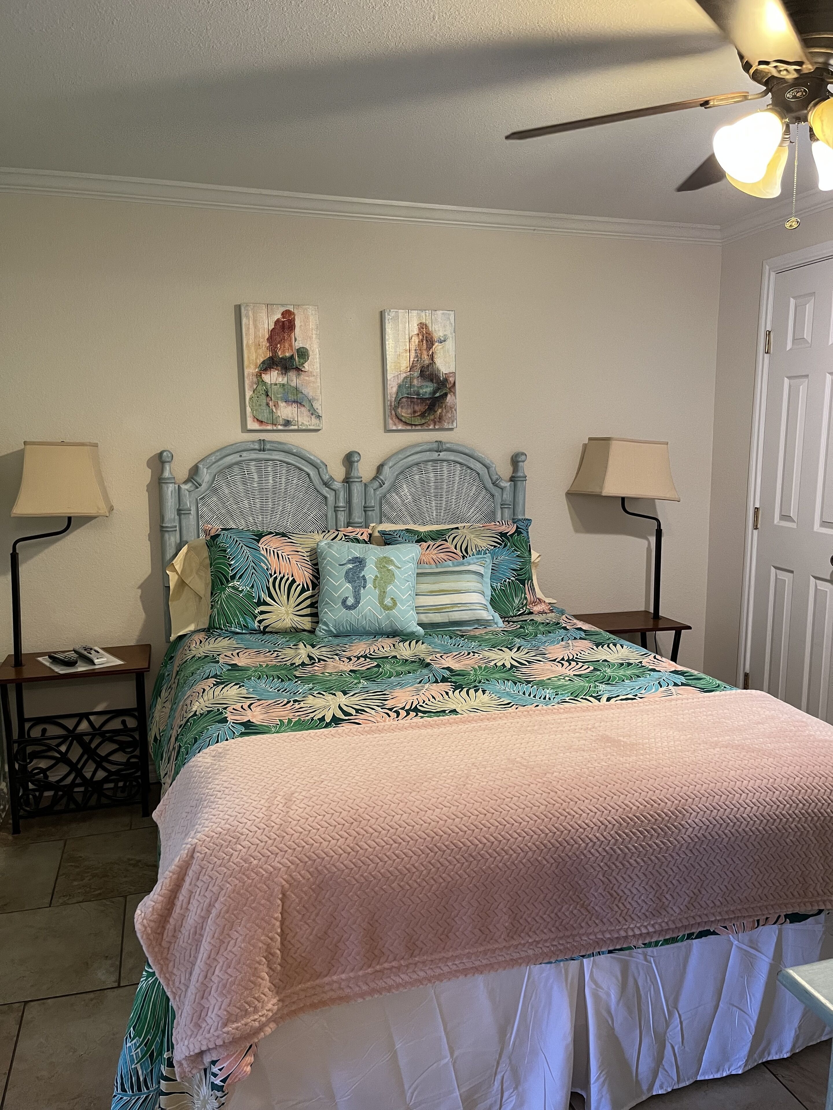 Un dormitorio con cama, dos lámparas de pared, un ventilador de techo y dos obras de arte en la pared.