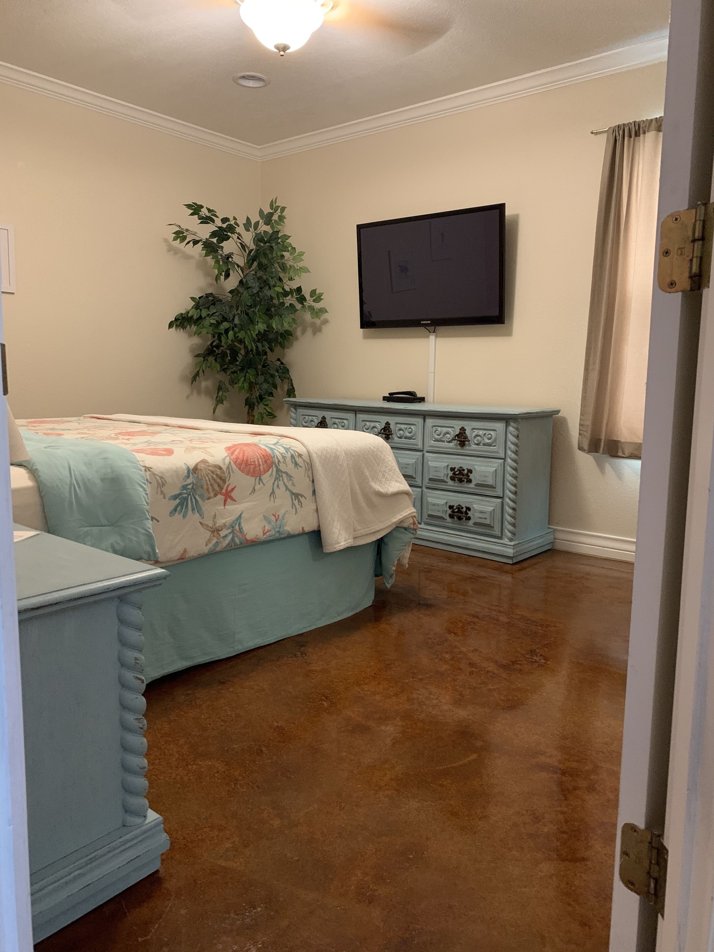 A bedroom with a bed, dresser, television, and a potted plant.