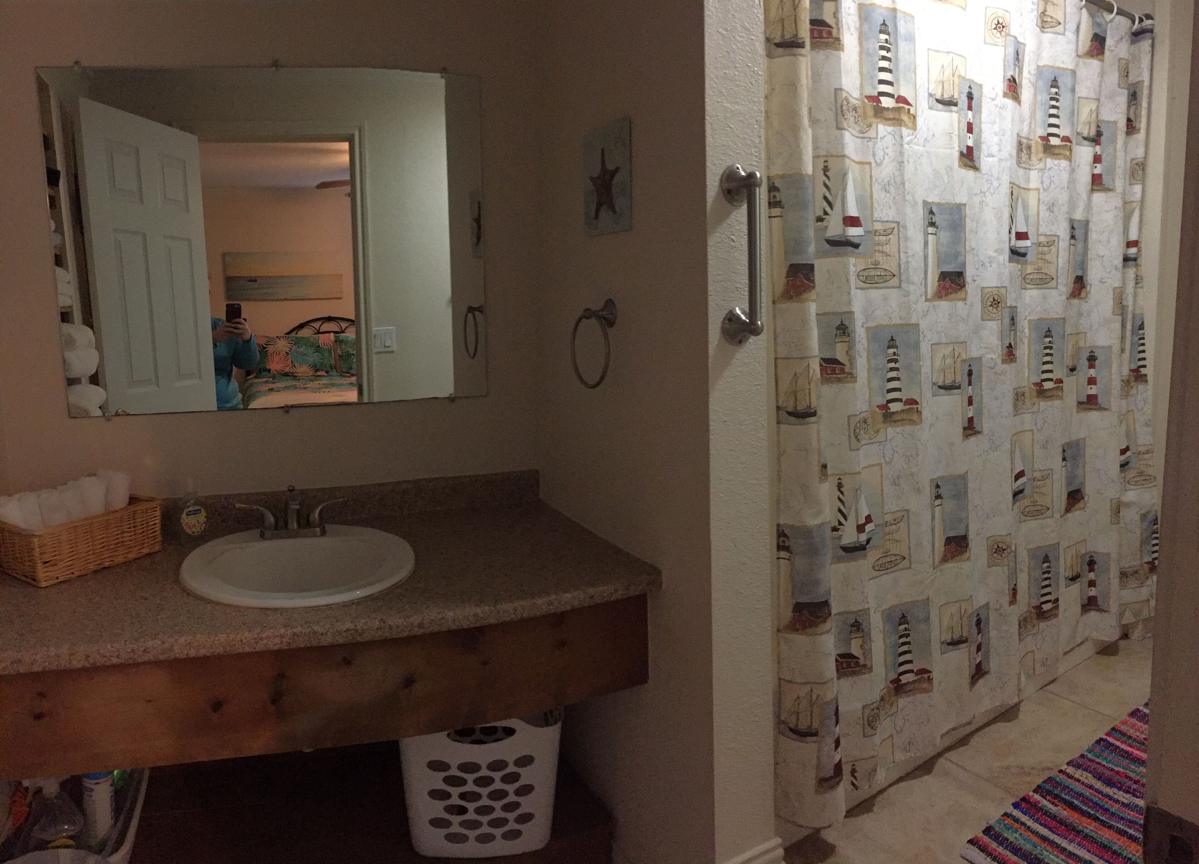 A bathroom with a wooden vanity, a white sink, a mirror, and a shower curtain with nautical designs.