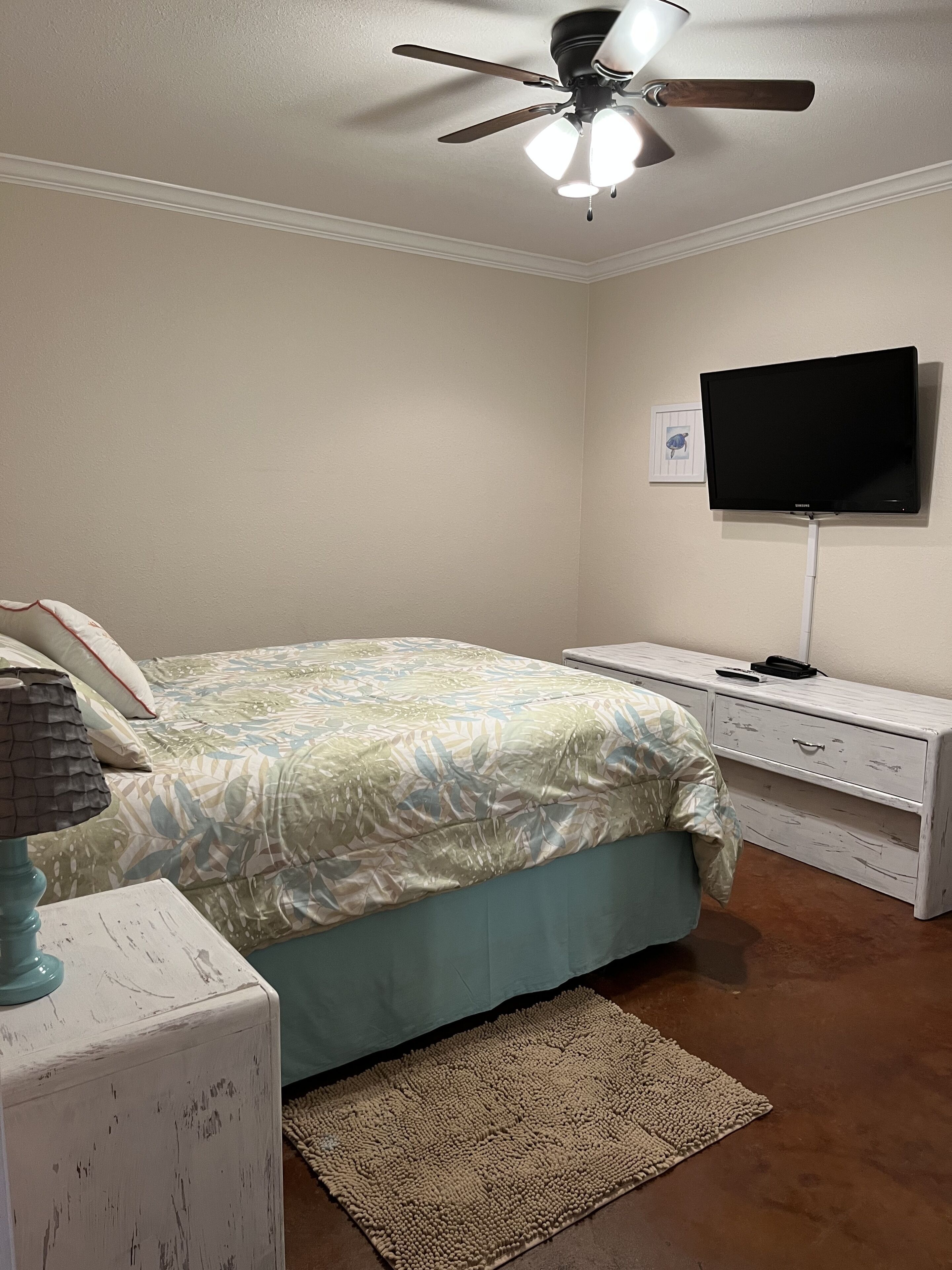 A bedroom with a bed, a TV, a ceiling fan, and a nightstand.