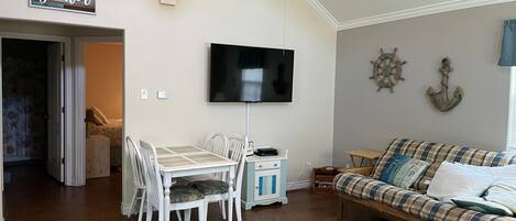 Una sala de estar con televisor, una mesa de comedor con sillas, un sofá y un letrero que dice 'gather'.