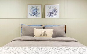 A bedroom with a bed, two framed floral paintings on the wall, and a pillow with the text "STAY AWAY."