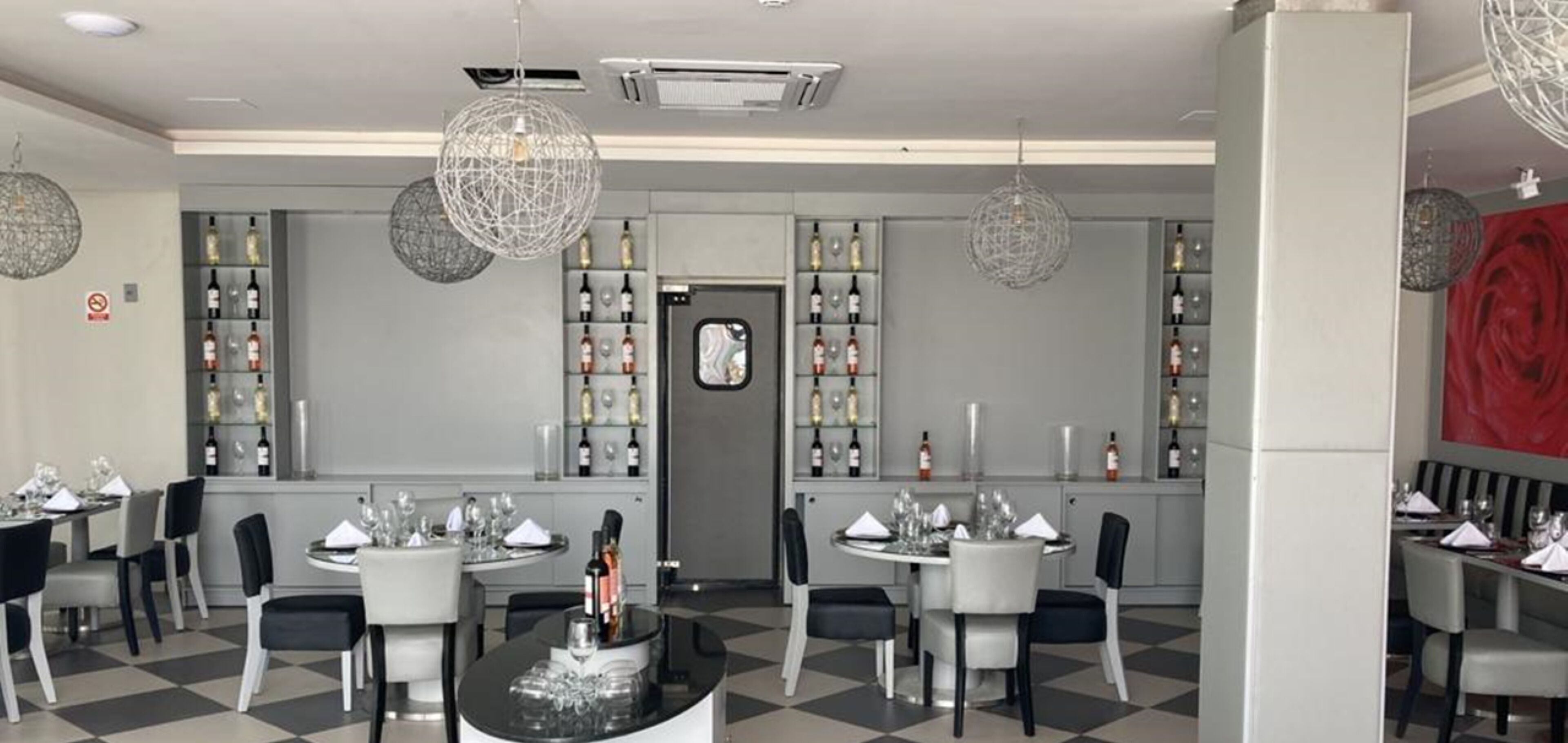 A modern restaurant interior with checkered flooring, round tables, and hanging spherical light fixtures.