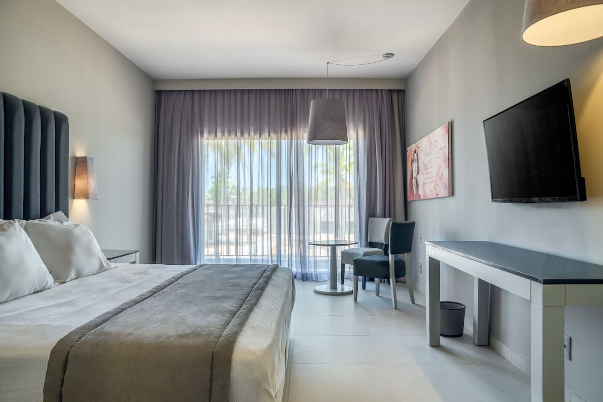 Una habitación de hotel moderna con cama, escritorio, silla, televisor y ventana con cortinas.