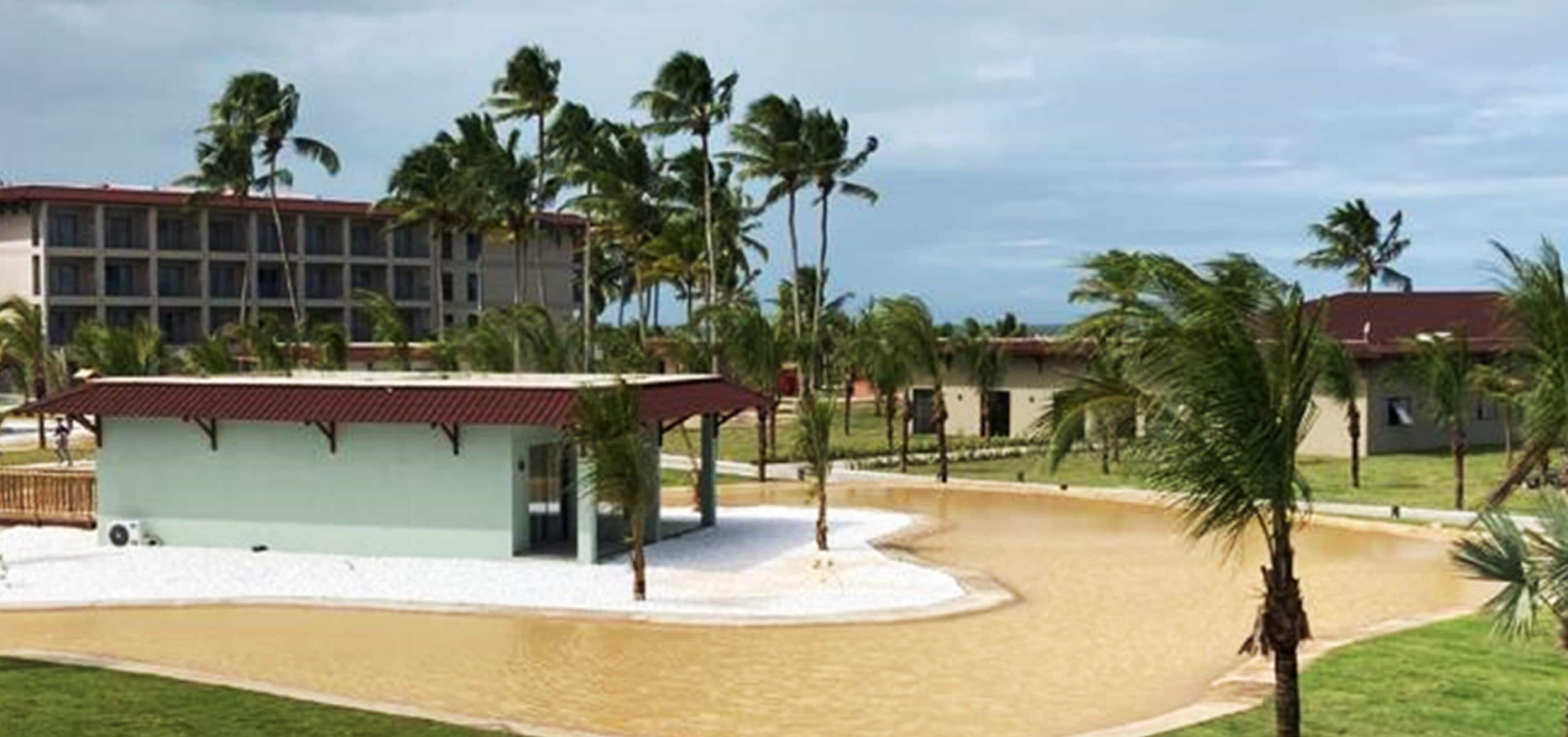 A resort with a pool, palm trees, and a building with a red roof.