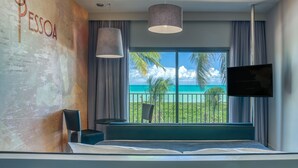 A modern hotel room with a large window offering a view of the ocean, a bed, a TV mounted on the wall, and a seating area with a chair. - Vila Galé Alagoas - All Inclusive (Barra de Santo Antonio)