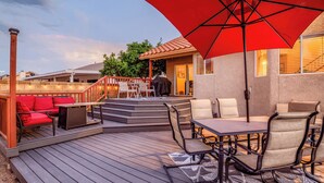 Une terrasse dotée de mobilier d’extérieur, d’un parasol rouge et d’un espace barbecue abrité.
