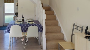 A dining area with a table set for four, a staircase, and a chair with a phone on it. - 2 bedroom accommodation in Falmouth (Falmouth)