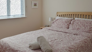 A neatly made bed with a floral-patterned bedspread, a wooden headboard, and a bedside table with a lamp. - 2 bedroom accommodation in Falmouth (Falmouth)
