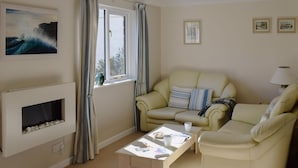 A living room with a beige sofa, a coffee table, a fireplace, and a window with curtains. - 2 bedroom accommodation in Falmouth (Falmouth)