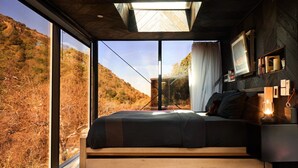 A bedroom with a large window, a bed, a bedside table with a lamp, and a wall-mounted TV. - Paradise Ranch Inn Stellar House Hot-Tub,Sauna . (three rivers)