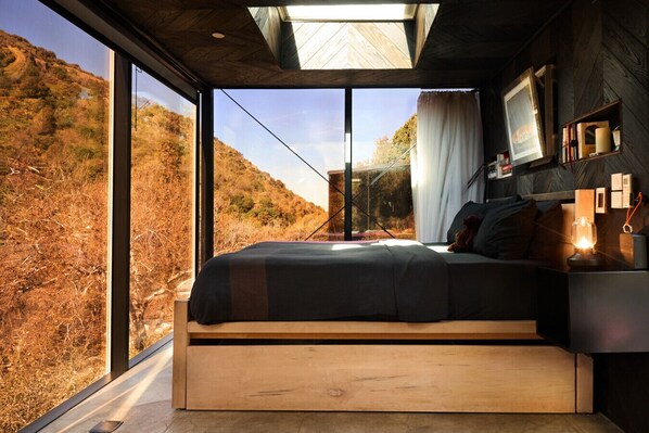 A bedroom with a large window, a bed, a bedside table with a lamp, and a wall-mounted TV. - Paradise Ranch Inn Stellar House Hot-Tub,Sauna . (three rivers)