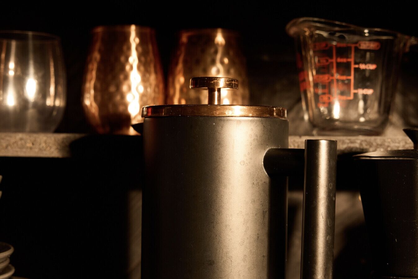 A kitchen counter with a stainless steel pot, a measuring cup, and two copper mugs.