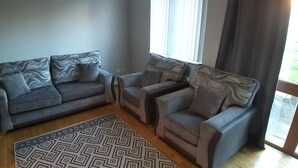 Een woonkamer met twee grijze banken, een kamerbreed tapijt en een groot raam met gordijnen.