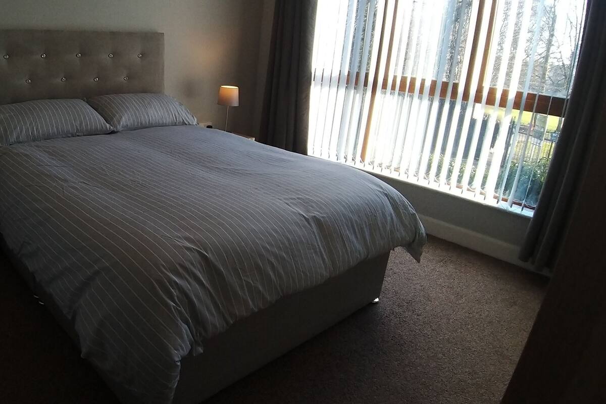 A neatly made bed with striped bedding, two bedside lamps, and a window with blinds.