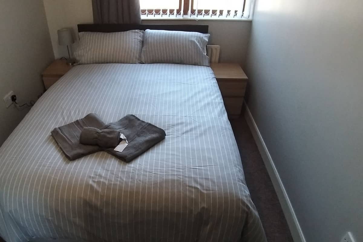 A neatly made bed with striped bedding, a bedside lamp, and a power outlet on the wall.
