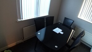 Een vergaderruimte met een zwarte tafel, vier stoelen en twee ramen met zonwering.