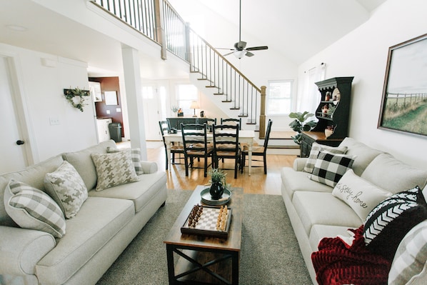 A spacious living room with a staircase, a coffee table with chess pieces, and a cozy fireplace.