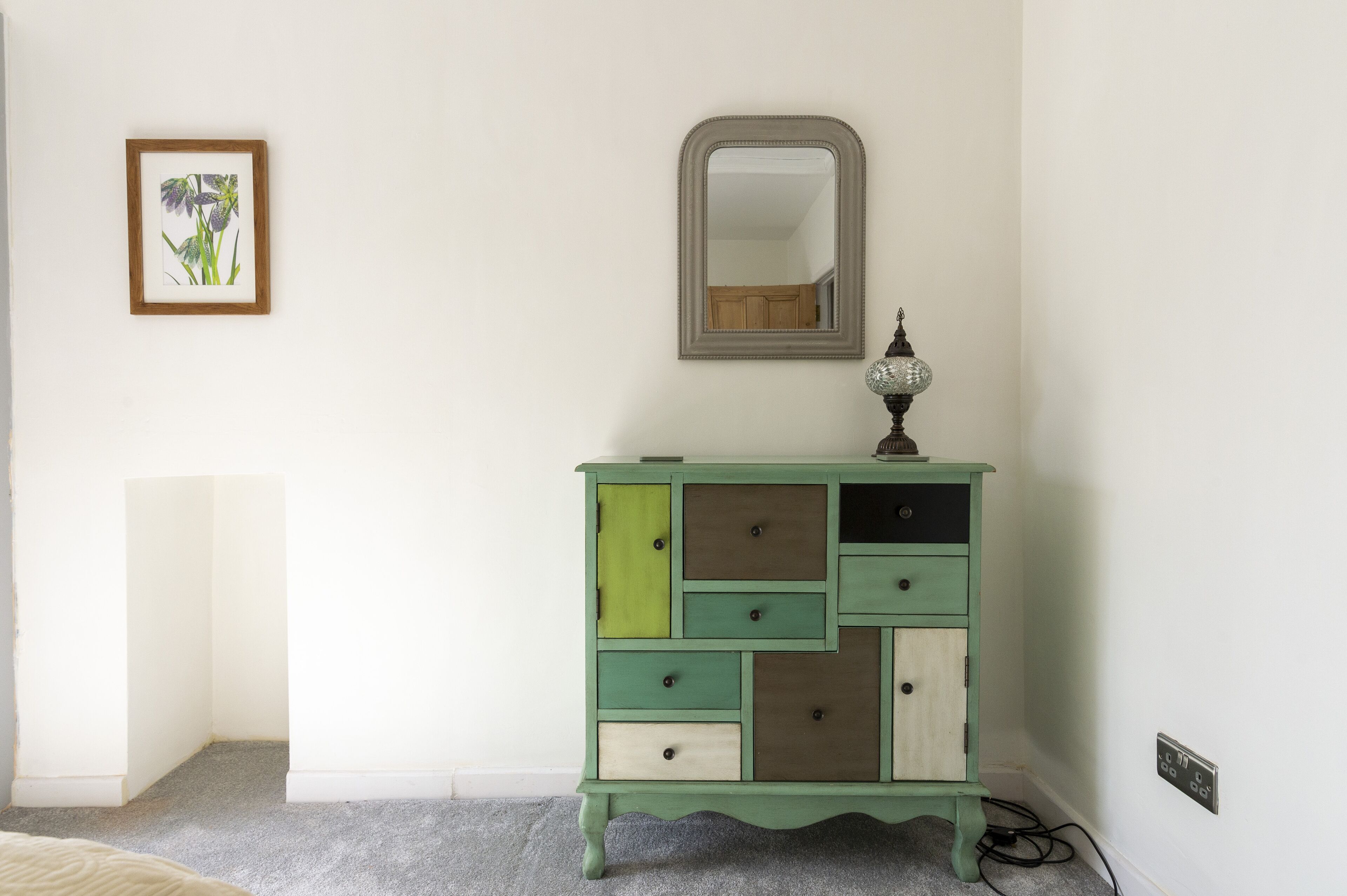 A green dresser with multiple drawers and a mirror above it.