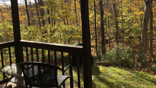 A wooden deck with a glass table and metal chair, overlooking a forest with autumn foliage. - Great Location, walk to the Flume 1.5 mi and trailheads (Lincoln)