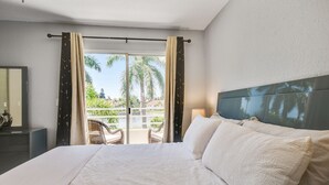 Ett hotellrum med en stor säng, en sänggavel och utsikt över palmer och en pool genom fönstret.