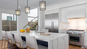 A modern kitchen with a large island, stainless steel appliances, and pendant lighting. - Brand New Luxury Beach Home (Newport Beach)