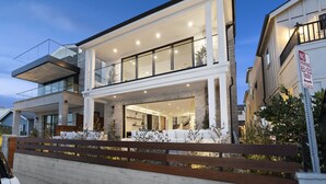 A modern two-story house with a balcony, large windows, and a wooden fence. - Brand New Luxury Beach Home (Newport Beach)