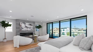 A modern bedroom with a large window, a fireplace, and a sofa. - Brand New Luxury Beach Home (Newport Beach)