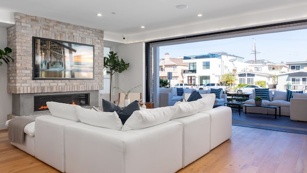 A modern living room with a white sofa, a fireplace, and a large window overlooking a residential area. - Brand New Luxury Beach Home (Newport Beach)