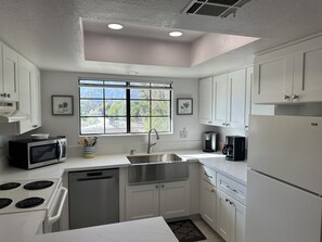 A modern kitchen with white cabinets, a stainless steel sink, a microwave, a dishwasher, and a refrigerator.