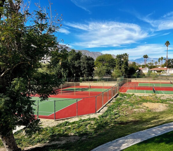 A tennis court complex with multiple courts, surrounded by trees and a mountain backdrop.