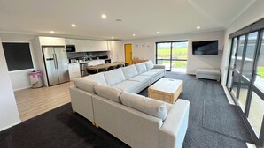 A modern living room with a sectional sofa, a coffee table, and a kitchen area with a refrigerator and stove. - Yellow Door (Ohakune)