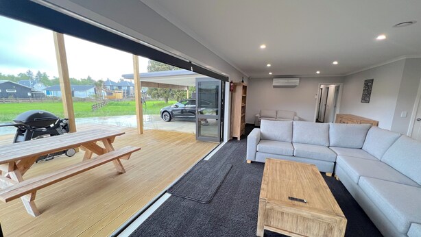 A modern living area with a wooden deck, a sofa, a coffee table, and a grill. - Yellow Door (Ohakune)