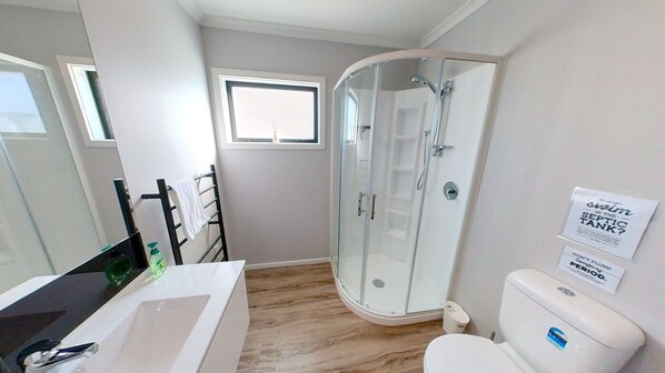 A modern bathroom with a glass shower enclosure, a white toilet, and a large mirror. - Yellow Door (Ohakune)
