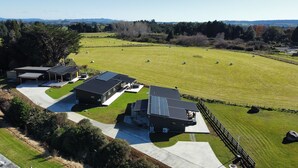 A modern building with solar panels, a large grassy field with hay bales, and a hilly landscape in the background. - Yellow Door (Ohakune)