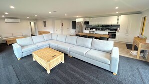 A modern living room with a sectional sofa, a wooden coffee table, and a kitchen area with white cabinets and appliances. - Yellow Door (Ohakune)
