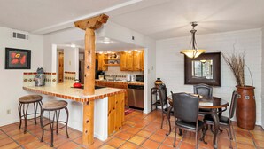 Una cocina con armarios de madera, una isla central con taburetes, una mesa de comedor con sillas y un jarrón grande.