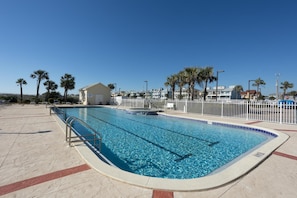 Relax by the rectangular pool surrounded by a white fence and palm trees.