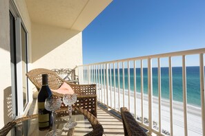 Un balcone con mobili in vimini, un tavolino in vetro e una bottiglia di vino.
